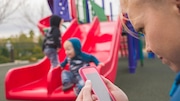 Woman stares at phone, kids play in background.