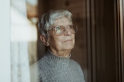 Portrait of an 79 years old woman in her modest home looking out the closed window. She had a not so easy life but looks back in peace and gratitude.